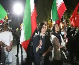 تصویر  -  تصویری متفاوت از دو دختر در تجمعات تهران؛ نوشته معنادار خطاب به ترامپ با پرچم حزب الله و جمهوری اسلامی ایران